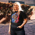T-shirt unisexe Dragon Flow – Édition France de H2O RESPIRO, noir, porté par une femme, avec un grand motif dragon bleu, rouge et doré sur le devant, devant une haie fleurie.
