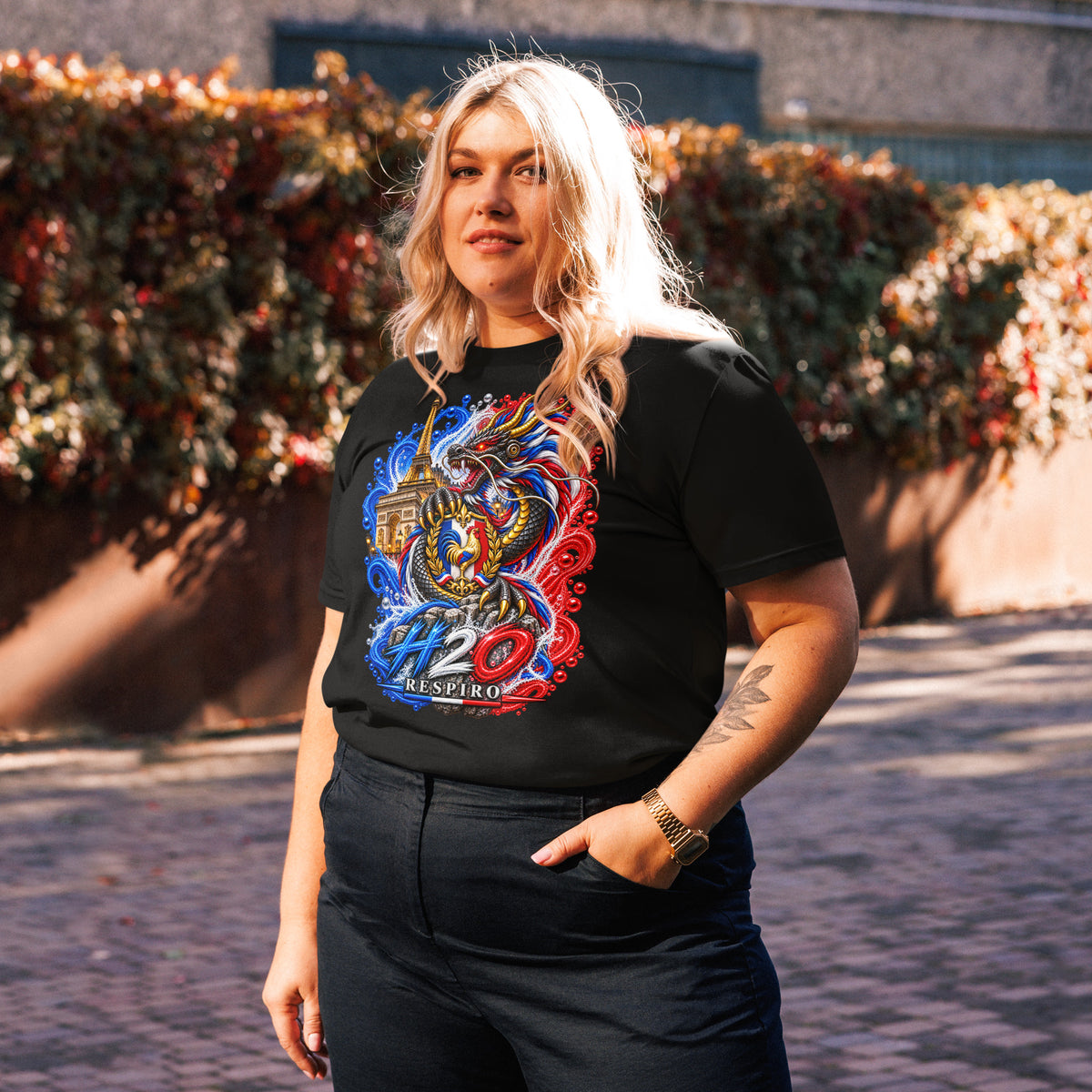 T-shirt unisexe Dragon Flow – Édition France de H2O RESPIRO, noir, porté par une femme, avec un grand motif dragon bleu, rouge et doré sur le devant, devant une haie fleurie.